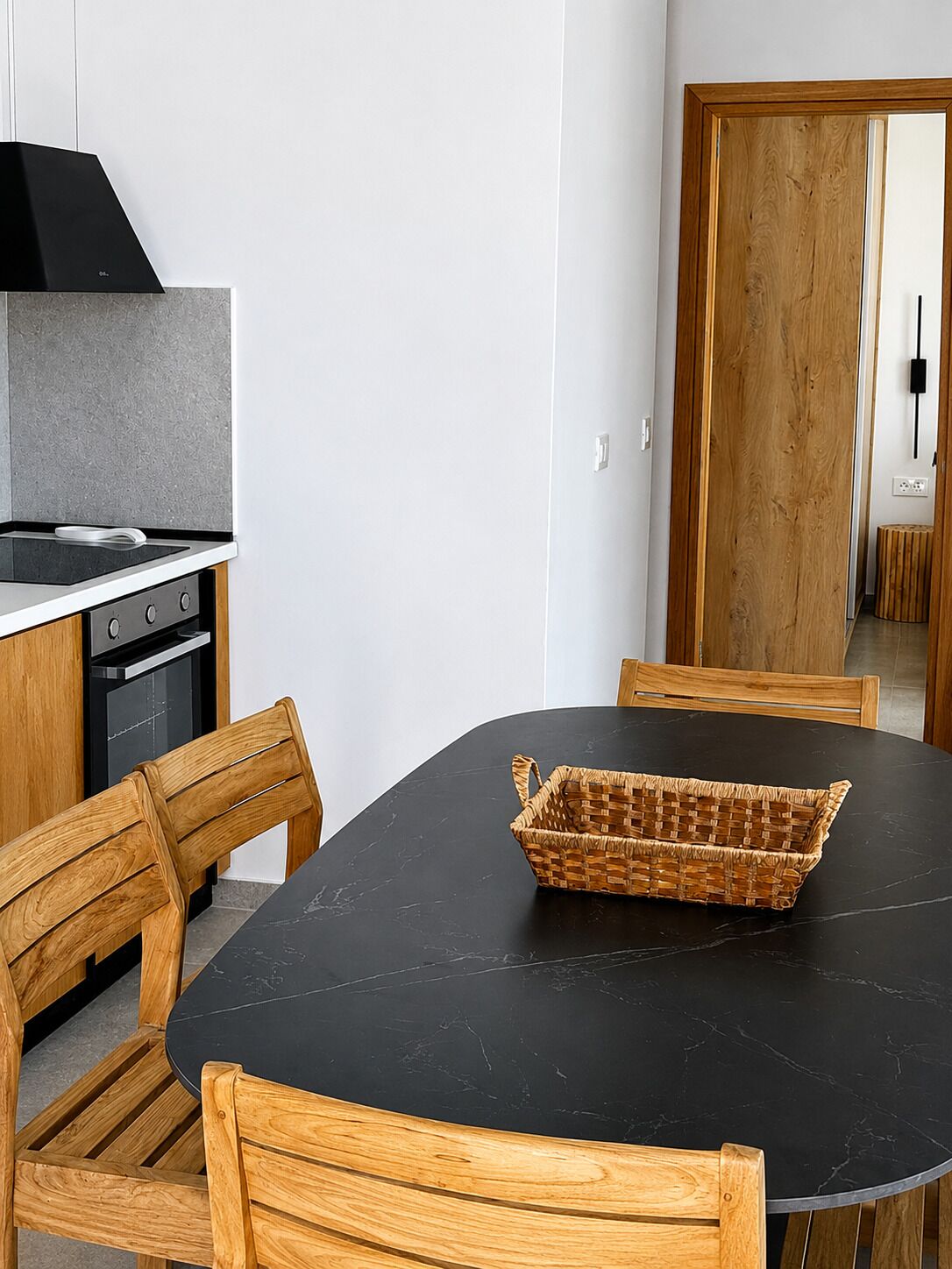 A modern kitchen with a black countertop, wooden chairs, and a woven basket on the table.