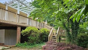Ein überdachter Außenbereich mit Holzterrasse, Backsteinmauer und einer Treppe, die zu einer höheren Ebene führt.