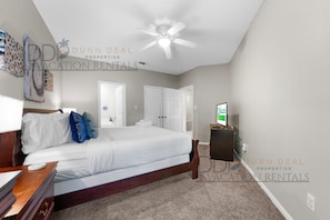 A bedroom with a bed, a ceiling fan, a TV, and a door.