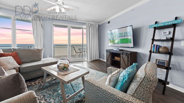 A modern living room with a large window, a ceiling fan, a flat-screen TV, and a view of the ocean.