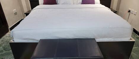Una cama bien tendida con un cabecero negro, un banco negro a juego y un tapete de colores con botones.
