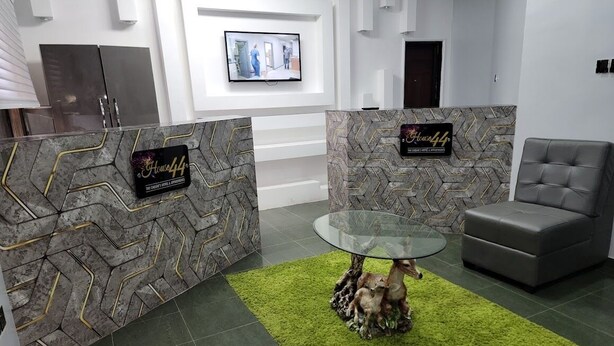 A reception area with a glass-top table, a green rug, and a grey sofa. - House 44 (Lagos)