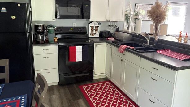 A modern kitchen with white cabinets, a black refrigerator, a microwave, an oven, a sink, and a coffee maker.