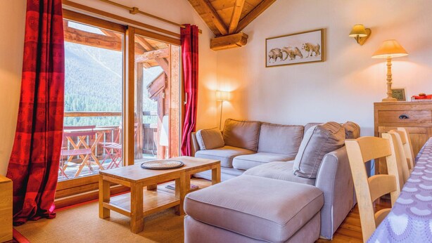 A cozy living room with a wooden ceiling, a sofa, a table, and a view of a wooden deck.