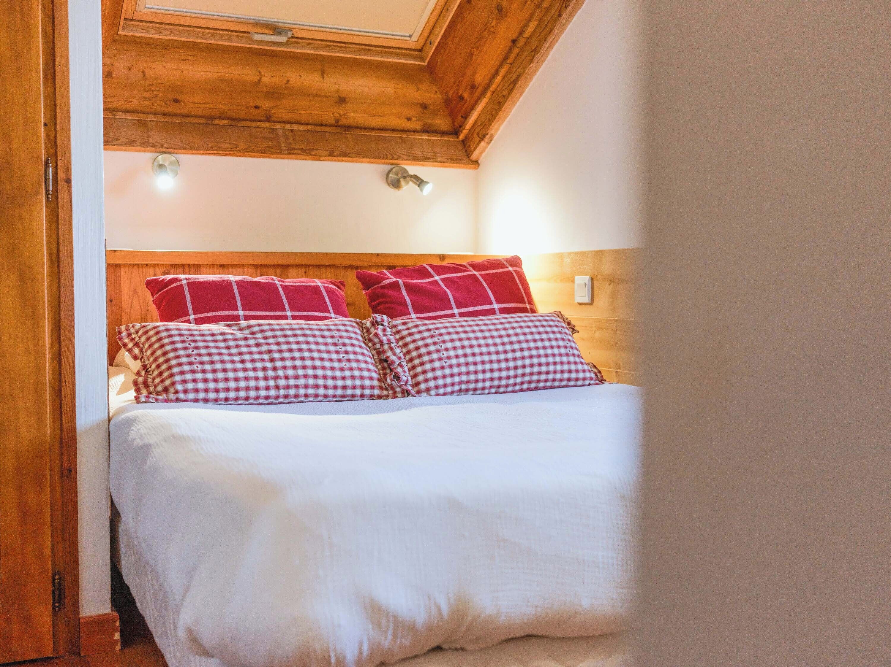 Ein Schlafzimmer mit Holzboden und einem Bett mit weißer Bettwäsche und rot-weißen Karokissen.