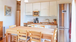 A modern kitchen with white cabinets, a stainless steel refrigerator, a wooden dining table with chairs, and pendant lighting.