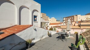 A rooftop terrace with a table and chairs, potted plants, and a view of the cityscape.