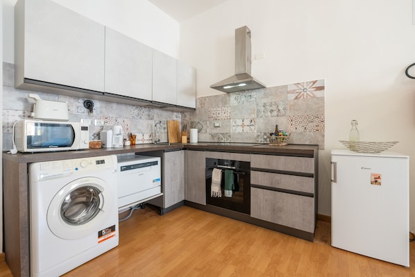A compact kitchen with a washing machine, microwave, oven, and a refrigerator.