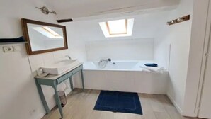Une salle de bain avec un puits de lumière, une baignoire, un lavabo et un miroir.