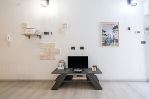A modern room with a flat-screen TV on a black TV stand, a framed picture on the wall, and a small shelf with items.