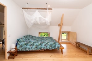 A bedroom with a bed, wooden bench, bedside table, and a window with a view of greenery.