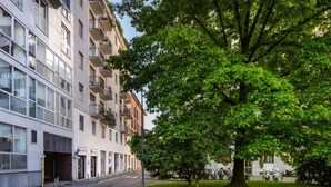 Un bâtiment moderne à étages, doté de balcons et orné d’un grand arbre à l’avant.