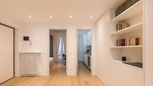 Un appartement moderne doté d’un plancher en bois, de murs blancs, d’une cuisine avec des meubles blancs et d’une bibliothèque remplie de livres.