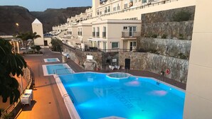 A swimming pool with a stone wall and a building with balconies in the background. - Cozy Home With Terrace and Access to Swimming Pool! (Mogan)