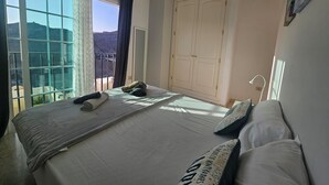 A bedroom with a large bed, a wardrobe, a ceiling fan, and a window with a view of a mountainous landscape. - Cozy Home With Terrace and Access to Swimming Pool! (Mogan)