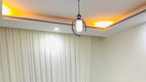 Una cama bien tendida con sábanas blancas y una toalla enrollada, un cabecero gris y una lámpara del techo.