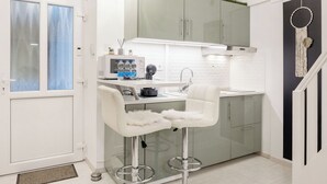 A modern kitchen with white cabinetry, a built-in microwave, and a white countertop. There are two white bar stools with fluffy seats and chrome bases. - Margaret Studio by the Danube near Margaret Island (Budapest)