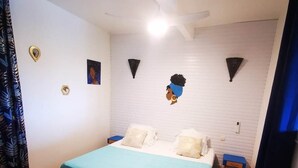A bedroom with a bed, a blue bedspread, a wooden floor, and a small rug. - Following the Horizon of the Balisiers (Sainte-Anne)