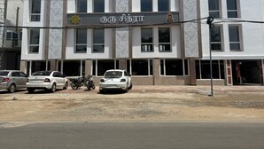 A multi-story building with a white facade and decorative leaf patterns. There are several cars and a motorcycle parked in front.