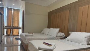 A hotel room with two beds, a wooden headboard, and a large window with curtains.