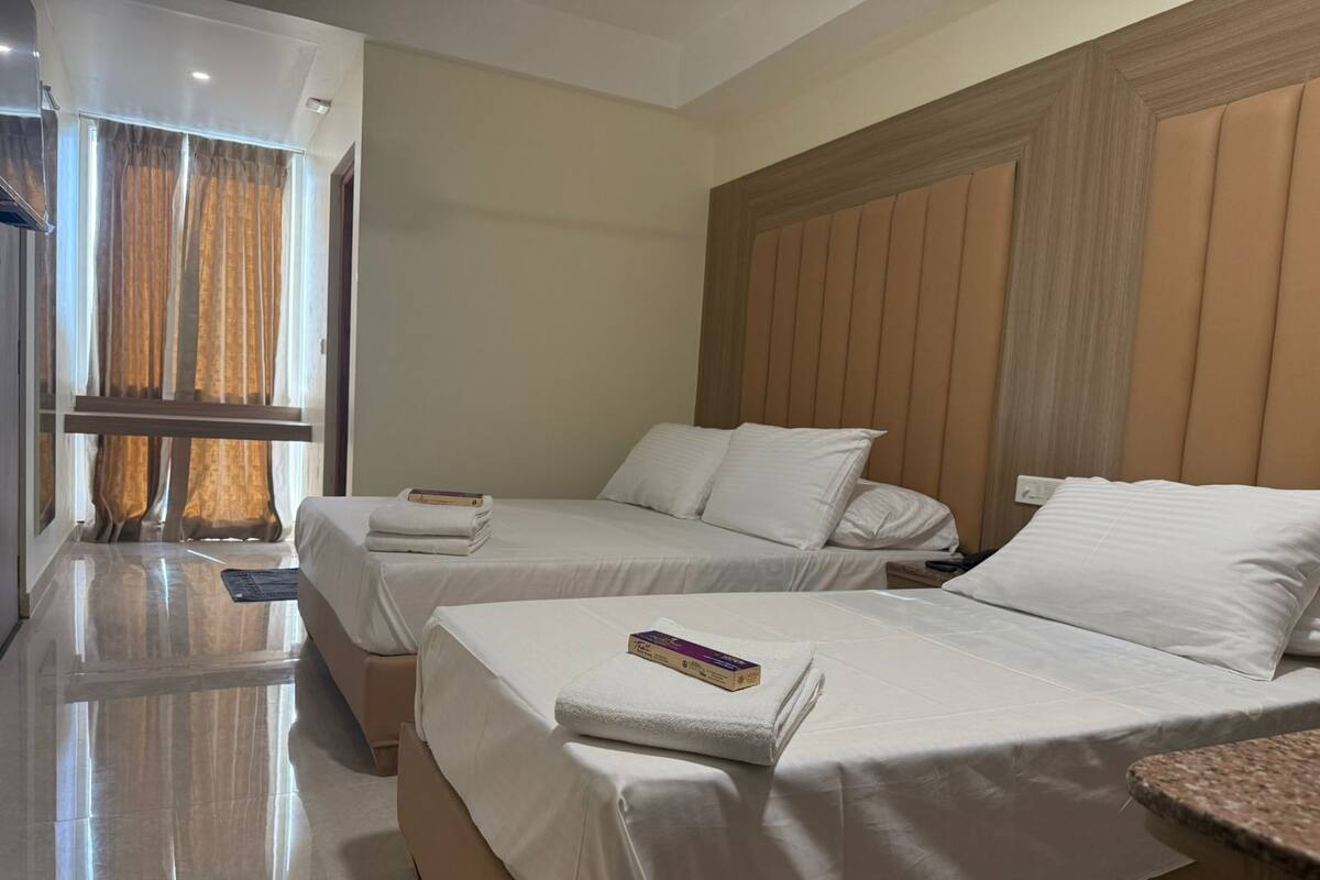 A hotel room with two beds, a wooden headboard, and a large window with curtains.