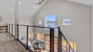 Une pièce spacieuse avec un plafond haut, un ventilateur de plafond et une vue sur une terrasse et les montagnes.