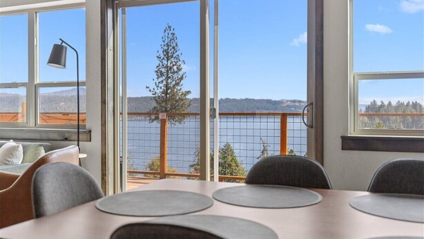 Une pièce dotée d’une grande table, de chaises, d’un bureau et offrant une vue sur un lac grâce à de grandes fenêtres.