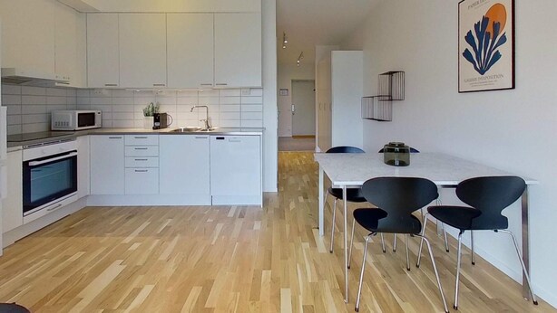 A modern kitchen with white cabinetry, a microwave, and a built-in oven. There is a dining area with a table and chairs. - 2 Person Holiday Park Home in Testby (Malmö)