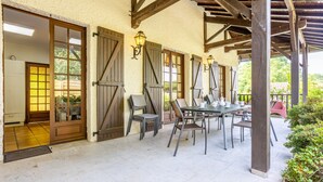 Un patio cubierto con mesa y sillas, vigas de madera y una puerta con paneles de vidrio.