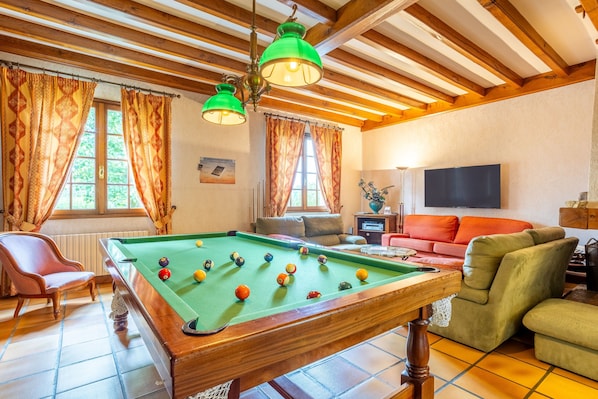 Une table de billard avec des billes, un canapé, un téléviseur et des poutres en bois au plafond.