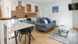 A compact living space with a kitchenette, a dining area, a grey sofa with cushions, a small table, and a TV mounted on the wall. - 3 Caroline Place (Fraserburgh)