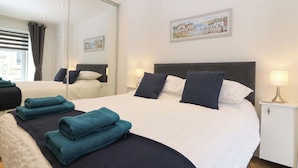 A hotel room with a large bed, a bedside table with a lamp, a mirror, and a painting on the wall. - 3 Caroline Place (Fraserburgh)