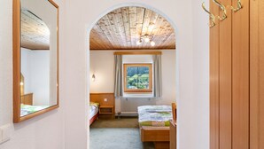 A bedroom with a wooden ceiling, a window with a view of greenery, a bed, a bedside table, and a mirror. - Room '6' with Mountain View, Shared Terrace and Wi-Fi (Hopfgarten in Tirol)