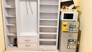 Un armario blanco con varios estantes, cajones y una barra para colgar, además de un microondas en la parte superior.