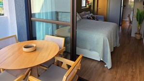 A modern room with a wooden dining table and chairs, a bed with a white duvet, and a sliding glass door leading to a balcony.