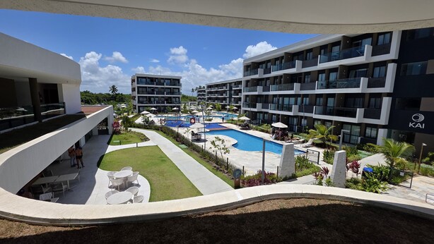 A modern hotel with a swimming pool, outdoor seating, and a view of the surrounding greenery.