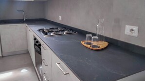 Cocina moderna con estufa a gas, una bandeja de madera con vasos y una botella grande.