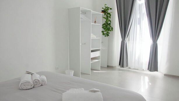 Una habitación de hotel moderna con una cama bien hecha, un armario blanco y una planta colgando del techo.