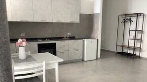 Una cocina moderna con armarios blancos, una mesa de comedor blanca y un refrigerador pequeño.
