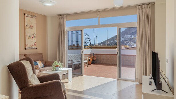 A living room with a sofa, a coffee table, a TV, and a balcony with a view of the city and mountains.