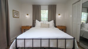 Ein Schlafzimmer mit einem großen Bett, zwei Nachttischen, einem Schminktisch und einem Fenster mit Vorhängen sowie einem Spiegel.