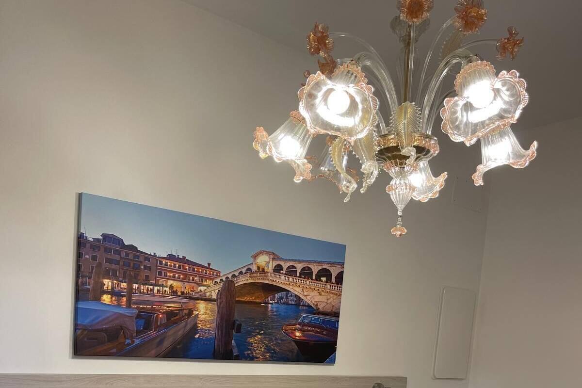 A hotel room with a bed, a painting of a bridge, and a chandelier.