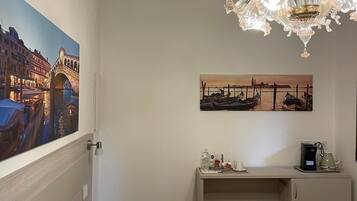 A hotel room with a bed, a desk with a coffee maker, and two paintings on the wall.