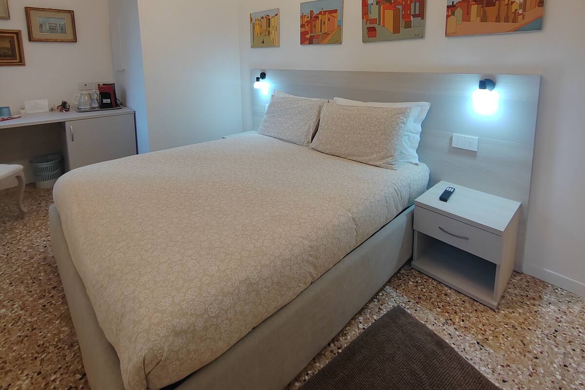 A bedroom with a bed, bedside tables, a desk, and a chandelier.