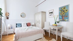 A bedroom with a bed, a round mirror, a white wardrobe, a small table with a vase, and a painting of sunflowers. - New Town Riverside Apartment (Hlavní město Praha)