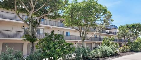 A multi-story residential building with balconies, a paved driveway, and surrounding greenery.