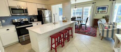 A modern kitchen with white cabinets, stainless steel appliances, and a central island with red stools.