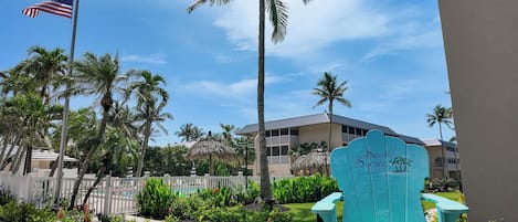 Un hotel frente a la playa con un letrero que dice "Sanibel Siesta On the Beach", rodeado de palmeras y una cerca blanca de piquete.