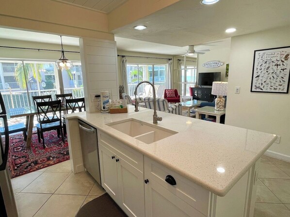 A modern kitchen with a large island, a dining area with chairs, and a view of the outdoors. - Sanibel Siesta on the Beach (Sanibel)
