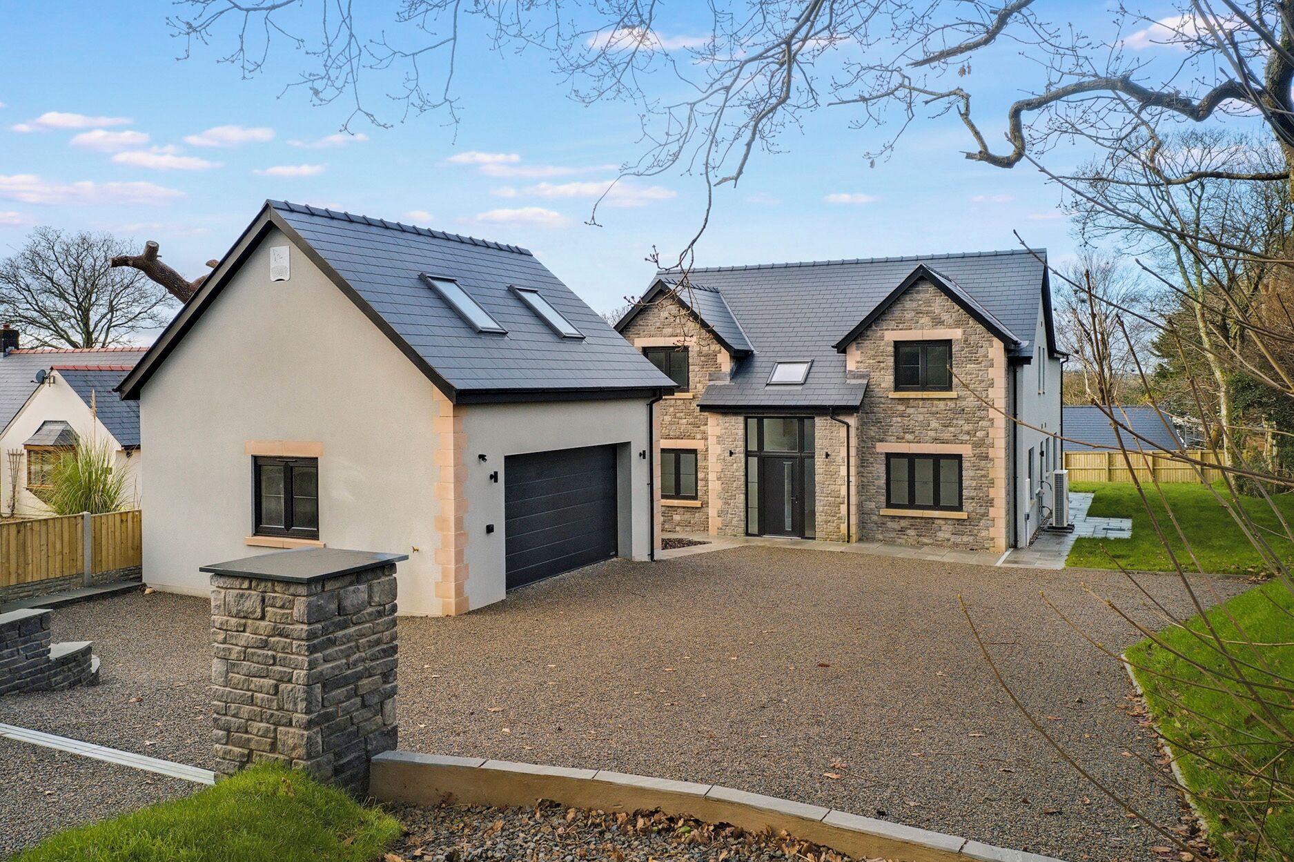 A modern two-story house with a stone facade, a black garage door, and a gravel driveway.